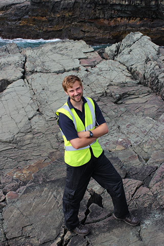 Photograph of Thomas Wong Hearing wearing field equipment and hi-vis jacket standing on the E surface at Mistaken Point, Newfoundland, Canada